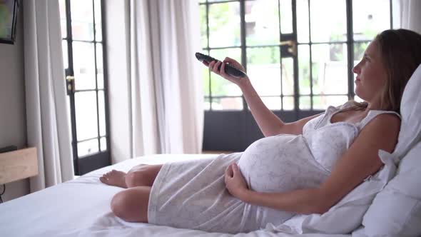 Pregnant woman resting on bed, watching TV