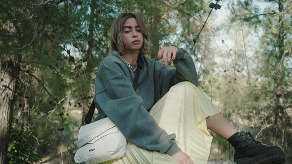 A beautiful woman pose for the camera sitting on giant rock wearing trendy outfit and hand bag in a