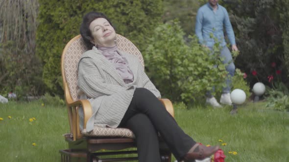 Portrait Adult Woman Sitting on the Lawn in the Rocking Chair Enjoying Sun Close-up. Adult Grandson