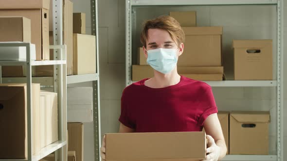 Man Wearing Red Tshirt Holding Parcels Employee of Warehouse in Medical Face Mask Holds Delivery