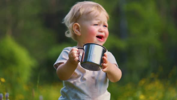 one year old baby spills liquid from a metal mug. The concept of walking outdoors,