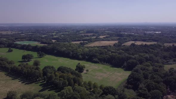 Drone aerial pan left to right over Trent Park North London UK, rural fields with small road in view