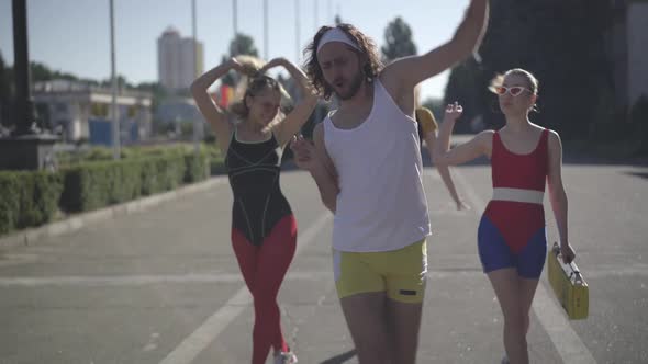 Positive Caucasian 1980s Man and Women Strolling in Sunlight Along Urban Road and Dancing To Disco