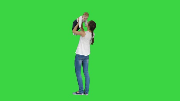 Young Mama Playing with Baby By Rising Him Up on a Green Screen, Chroma Key.