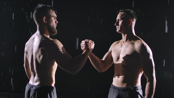 Two Focused Topless Men Shake Hands Amidst the Raindrops and Splashing Water. Picture Taken in the