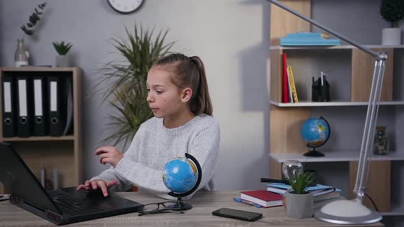 Modern Teen Girl Sitting at the Table and Typing on Computer in Searching the Neccessary Information