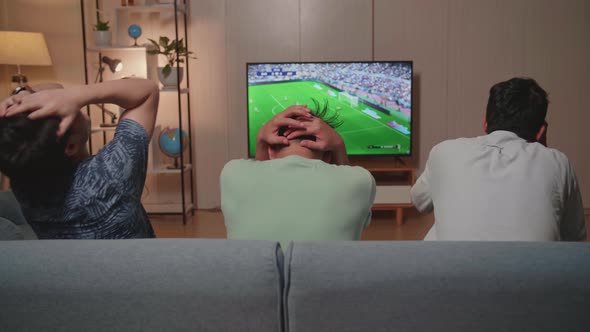 Back View Of Sad Male Friends Watching Soccer On Tv At Home