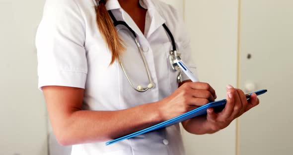 Female doctor with a stethoscope writing on a notebook while standing