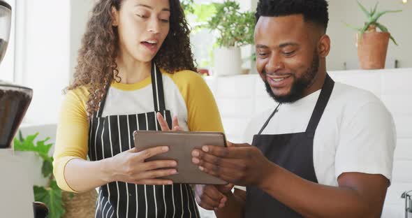 Happy african american male cafe owner and biracial female barista using tablet at cafe