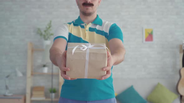 Young Mustachioed Male Delivery Man Courier with Gift Box in Hand