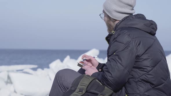 Handsome Blond Bearded Man Sitting Among the Ices Writing His Observations in a Notebook. Polar