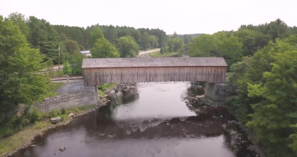 Aerial shot flying above the Piscataquls River and a wooden covered bridge in Maine.