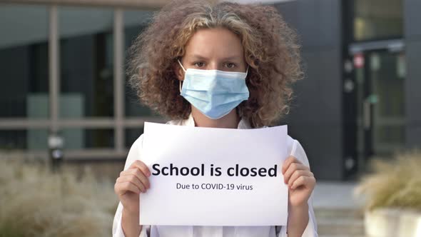 Schoolgirl Wearing a Medical Mask Holds a Sign SCHOOL IS CLOSED DUE TO COVID19 VIRUS