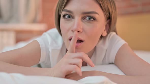 Close Up of Young Woman Putting Finger on Lips in Bed