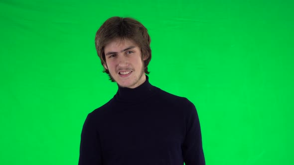 Portrait of Tall Slender Young Guy with Thick Hair Is Looking Straight and Smiling on a Green Screen