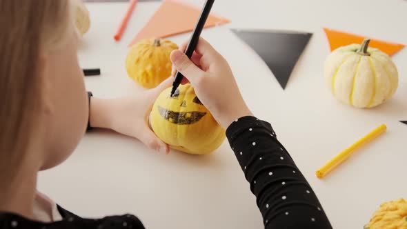 Little kid preparing for holiday Halloween. Hands of children drawing scary face on pumpkin