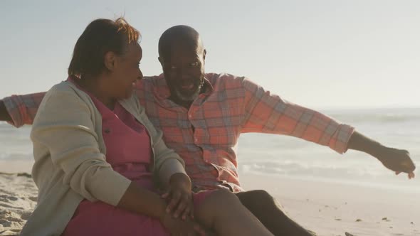 Smiling senior african american couple embracing and sitting on sunny beach
