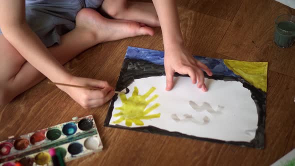 A Child on the Floor Draws a Drawing with Watercolors