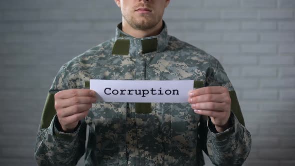Corruption Word Written on Sign in Hands of Male Soldier, Defense Industry Crime