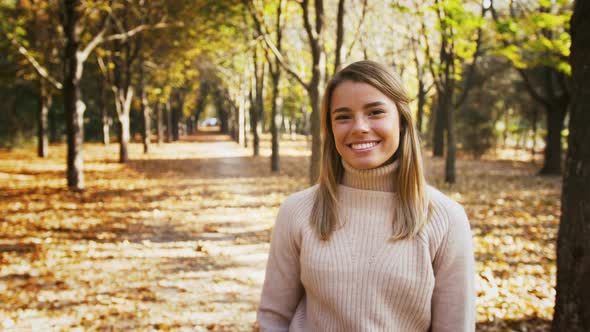 Young Woman is Smiling Straightening Hair and Looking at you While Posing at Walkway of Autumn Park