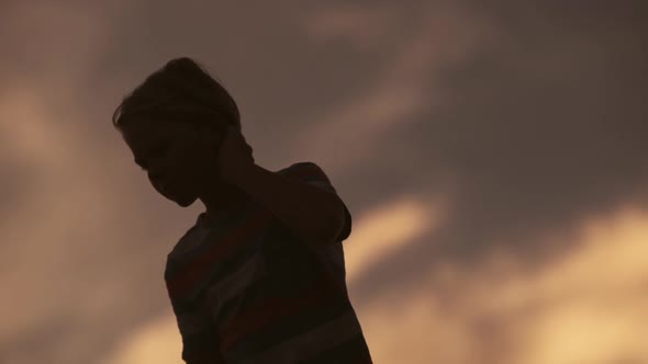 Silhouette of Young Handsome Boy Rejoicing Dancing in Field at Sunrise