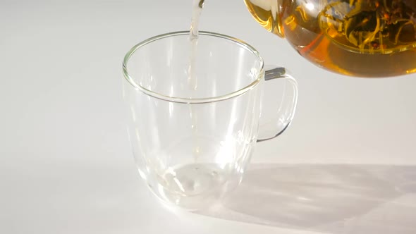 Hot Herbal Tea Pouring to Glass Cup on White Table Closeup Slow Motion