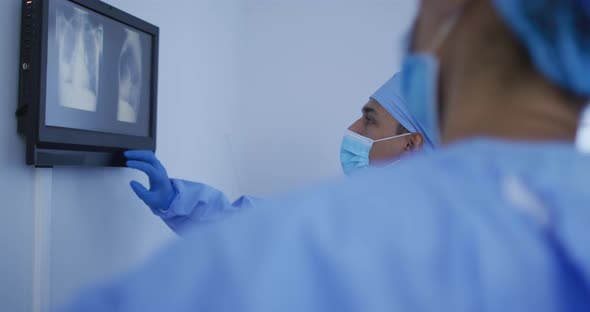 Mixed race male surgeon wearing protective clothing presenting x-ray on screen