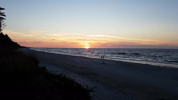 Sunset over the sea. Sandy beach. Peaceful colors. Relaxing scenery. Two people one the beach. Pan s