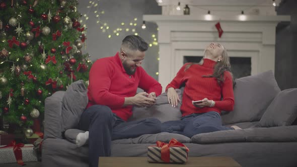 Happy Young Couple Relaxing on Couch in Decorated for Christmas Living Room