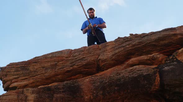 Athlete adjusting his rope on waist while standing on cliff