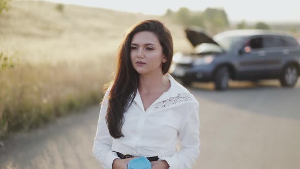 Thoughtful Girl with Cup in Hand Looks Out at Broken Car Out of City