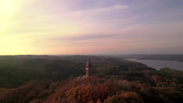 Drone Over Forest With Tower And Lake At Sunset