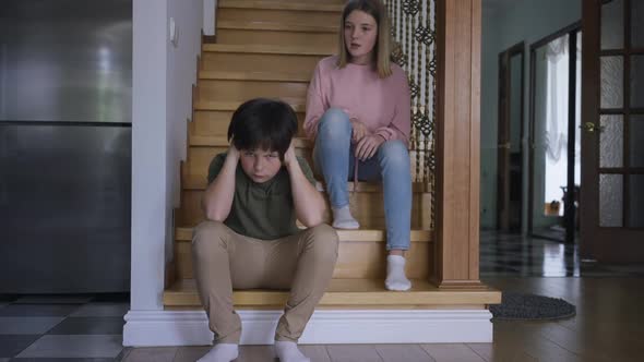 Wide Shot Portrait of Caucasian Brother Covering Ears with Hands As Sister Talking with Dissatisfied