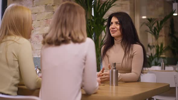 Excited Beautiful Slim Middle Eastern Woman Talking Sharing with Caucasian Friends Sitting in Cafe