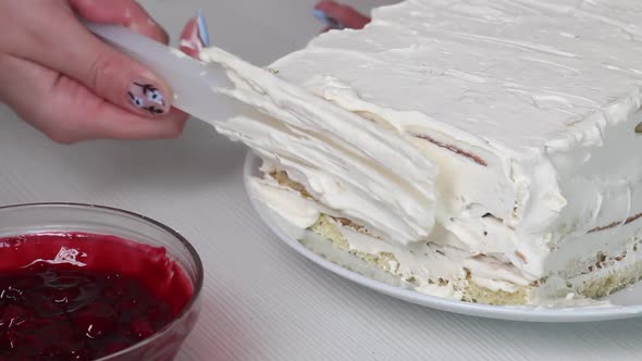 A Woman Smears A Biscuit Cake With Cream. Nearby Is A Container With Cherry Filling For The Cake