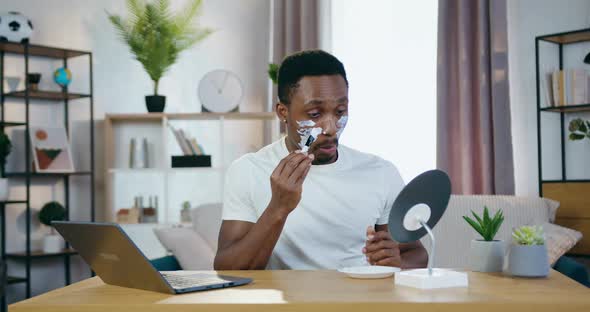 African American Sitting in front of Small Mirror and Applying Face mask