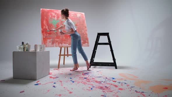 Young Female Artist Draws with a Brush on a Large Canvas in a White Room a Talented Artist Draws a