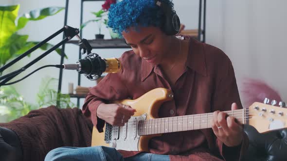 Young African American Woman Plays Guitar Sits on Sofa in Front of Microphone