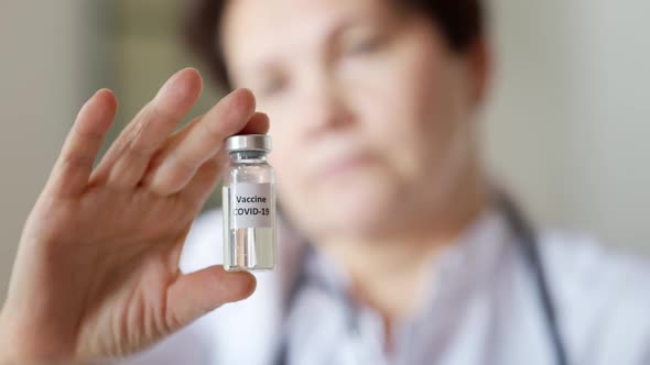 Closeup of Coronavirus Vaccine Jar in Female Caucasian Hand with Blurred Face of Serious Middle Aged