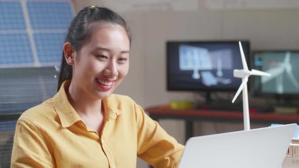 Asian Woman Smile While Working With A Laptop Next To The Model Of A Small House With Solar Panel