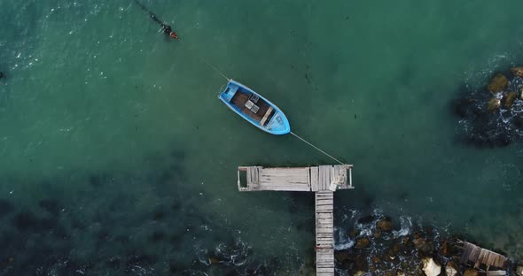 Aerial video of lonely fishing boat and wooden pier in turquoise ocean, sea. Top view