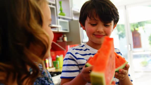 Siblings having watermelon in kitchen alt