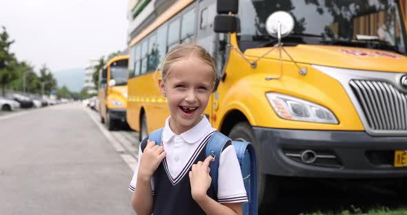 Schoolgirl Wearing School Uniform and Backpack and Standing Near Yellow Bus