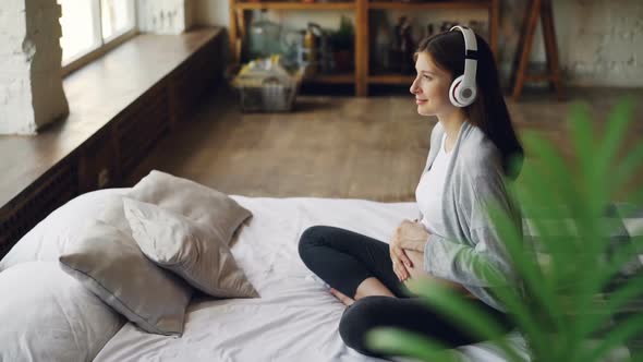 Happy Expecting Mother Is Caressing Her Tummy and Listening To Music Through Headphones Resting on