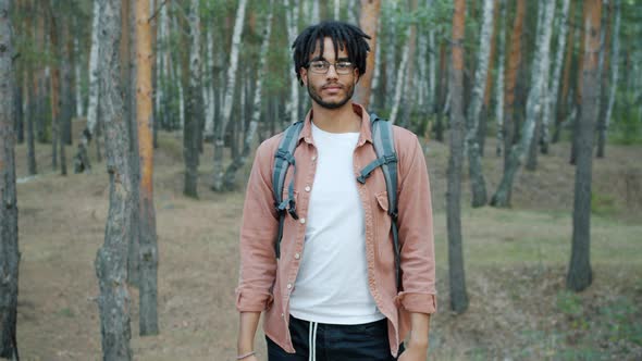 Portrait of AfroAmerican Man with Dreadlocks Standing in Forest with Backpack