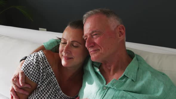 Caucasian senior couple hugging each other while sitting on the couch at home