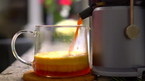 Close up electric juicer with nozzle pouring healthy vivid fruit juice into glass pitcher with layer