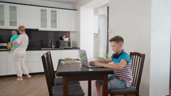 Teenager Studying on Laptop While Mother Cooking at Kitchen