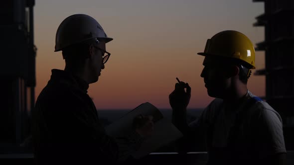 Construction Workers Having Discussion at Sunset. One Smokes.