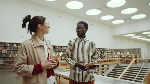 Multiethnic Man and Woman Walking in Library and Talking